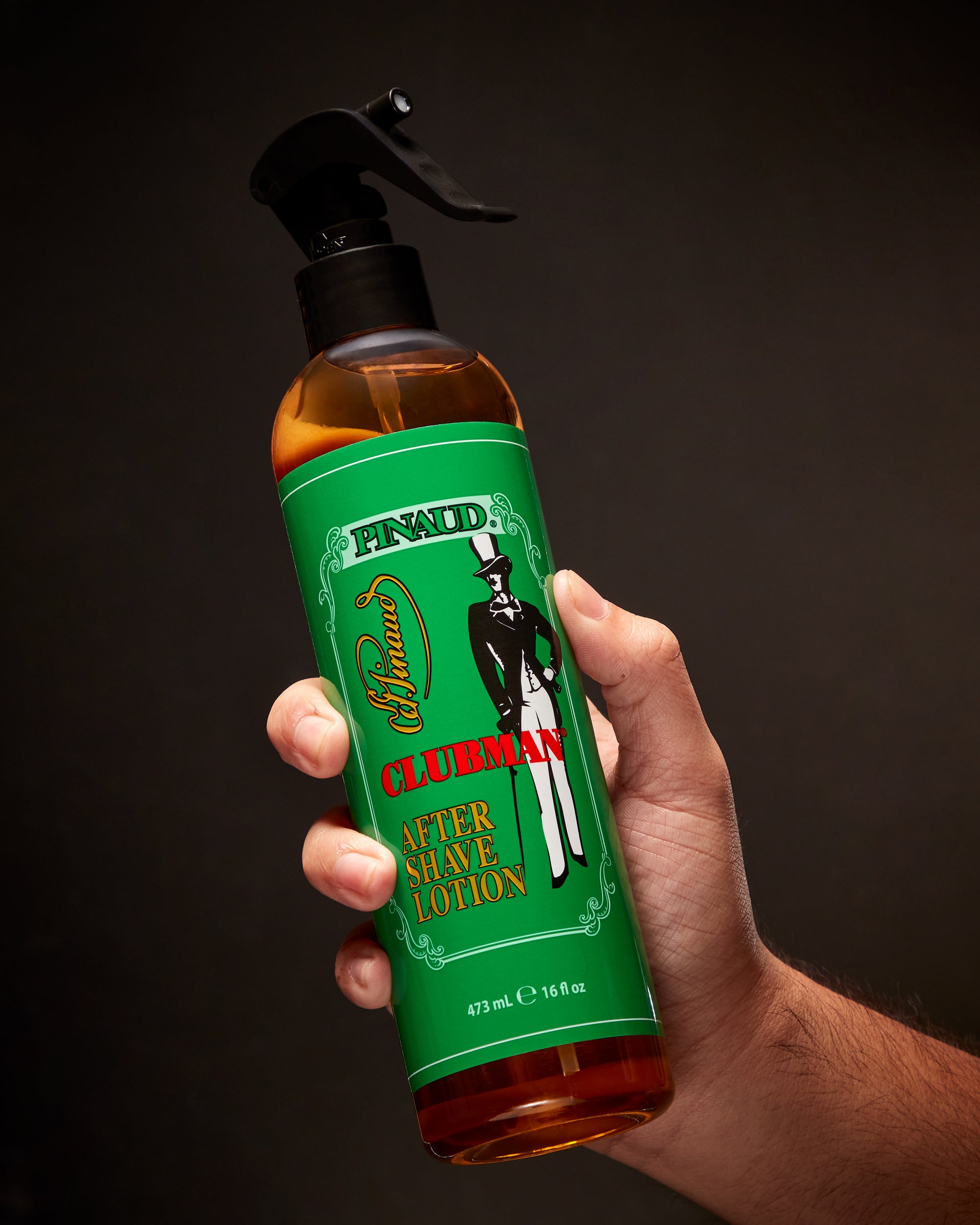 Hand holding a bottle of Clubman Aftershave Lotion against a dark background