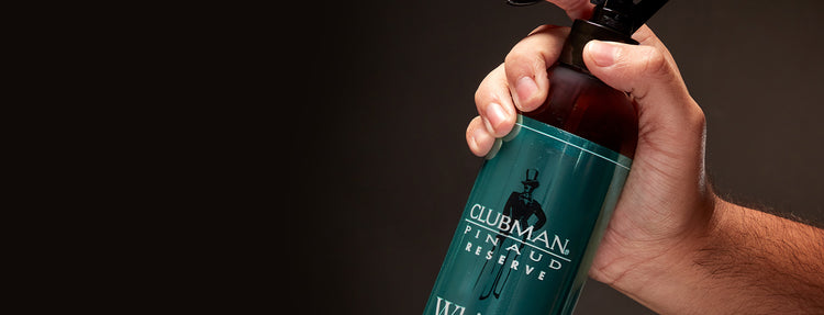 Hand holding a bottle of Clubman Pinaud Reserve against a dark background