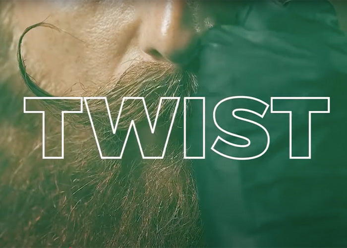 Bearded man styling his mustache with a gloved hand, with the word "TWIST" overlayed on the image.