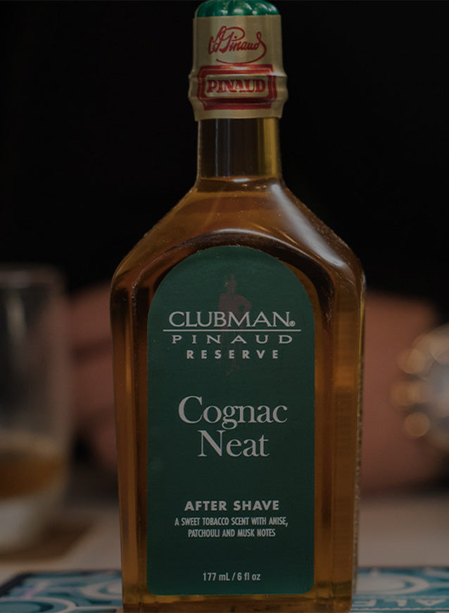 Bottle of of Clubman Pinaud Reserve Cognac Neat on top of a table and a persons hand and watch barely visible in the background