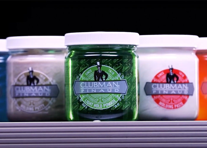 Close-up of Clubman Pinaud hair styling pomades in various colors, featuring Light Hold Pomade in a green jar.